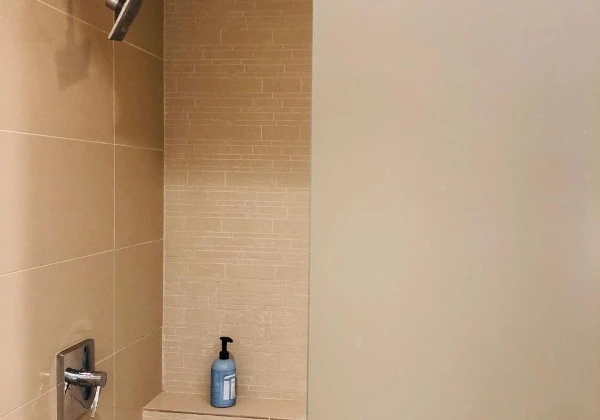 Tiled shower alcove with a wall-mounted shower head and a pump bottle on a recessed shelf