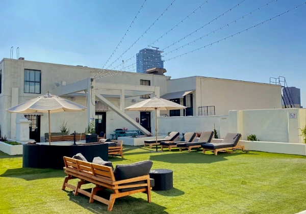 Kaqun LA rooftop terrace with green turf, lounge chairs, umbrellas and city buildings
