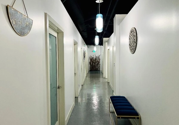 Kaqun LA corridor with frosted suite doors, hanging lights and a blue upholstered bench